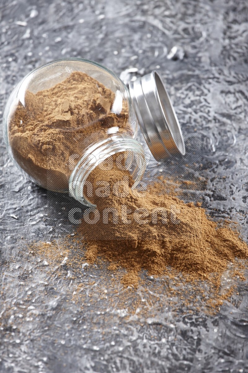 Flipped herbal glass jar full of cinnamon powder on textured black background