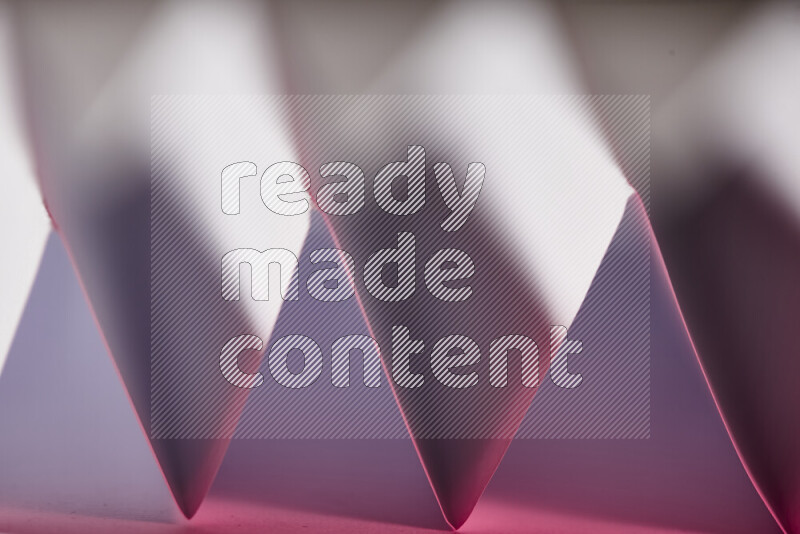 A close-up abstract image showing sharp geometric paper folds in white and pink gradients