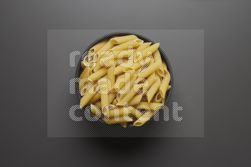 Penne pasta in a pottery bowl on grey background