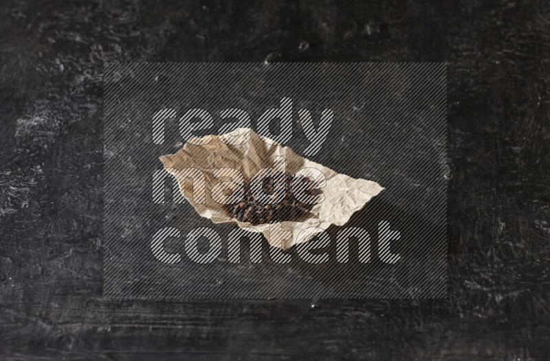 Cloves in crumpled piece of paper on a textured black flooring