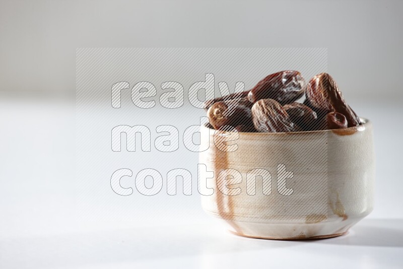 A beige ceramic bowl full of dried dates on a white background in different angles