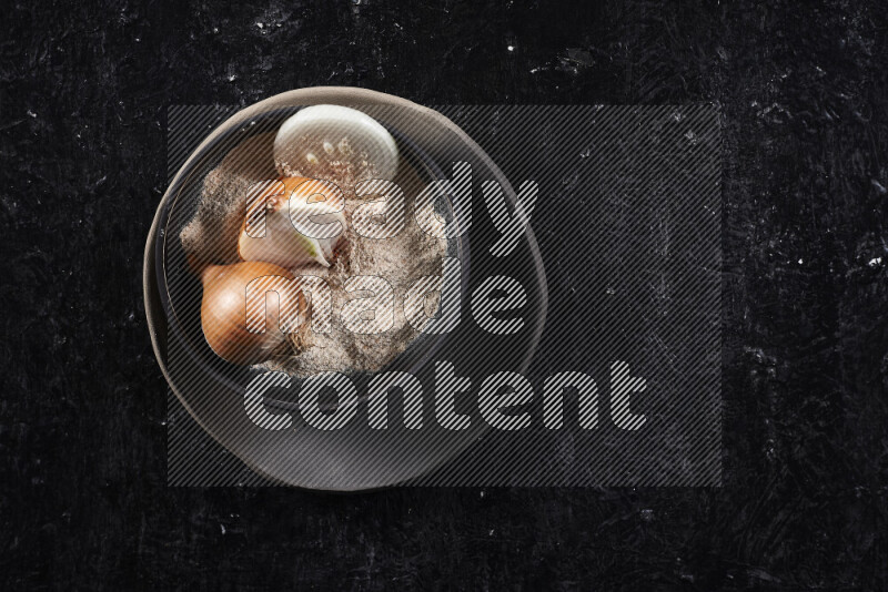 A black pottery bowl full of onion powder and some onion all on a pottery plate on black background