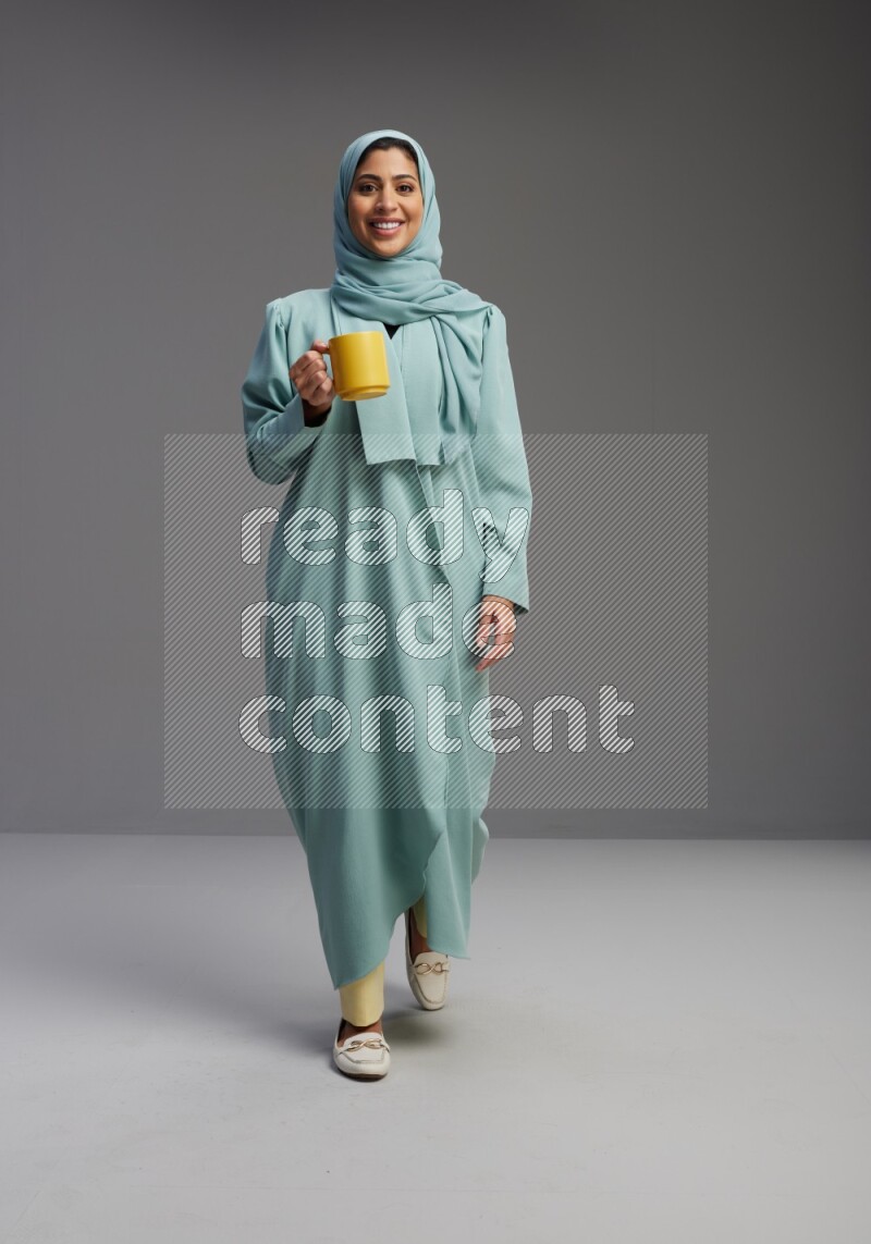 Saudi Woman wearing Abaya standing  holding a mug on Gray background