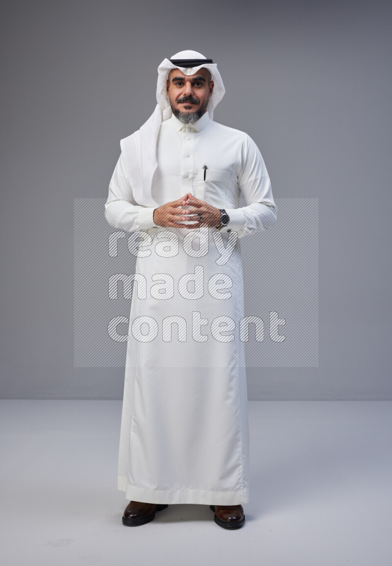 Saudi man Wearing Thob and white Shomag standing interacting with the camera on Gray background