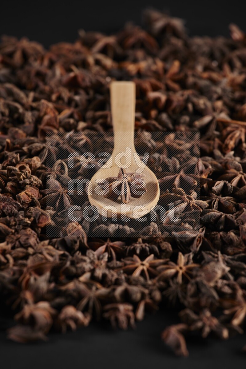 Star Anise in a wooden spoon on more stars anise filling the frame on black flooring