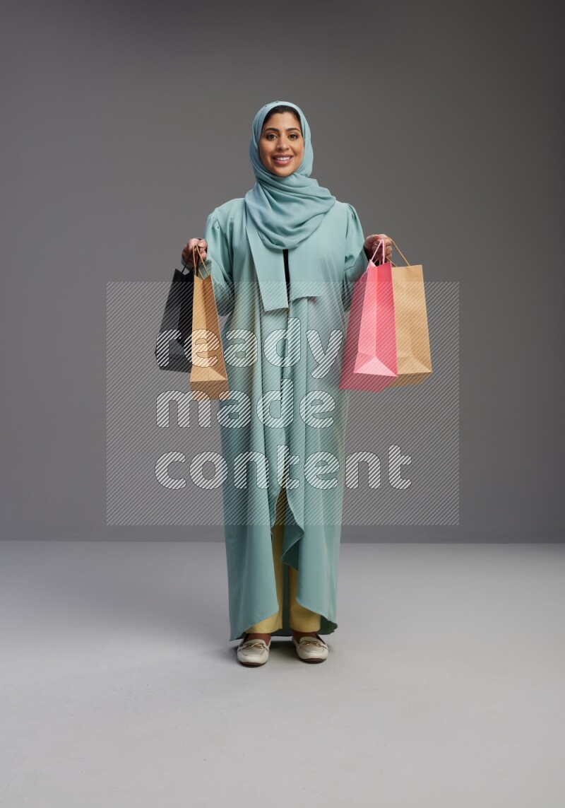 Saudi Woman wearing Abaya standing holding shopping bag on Gray background