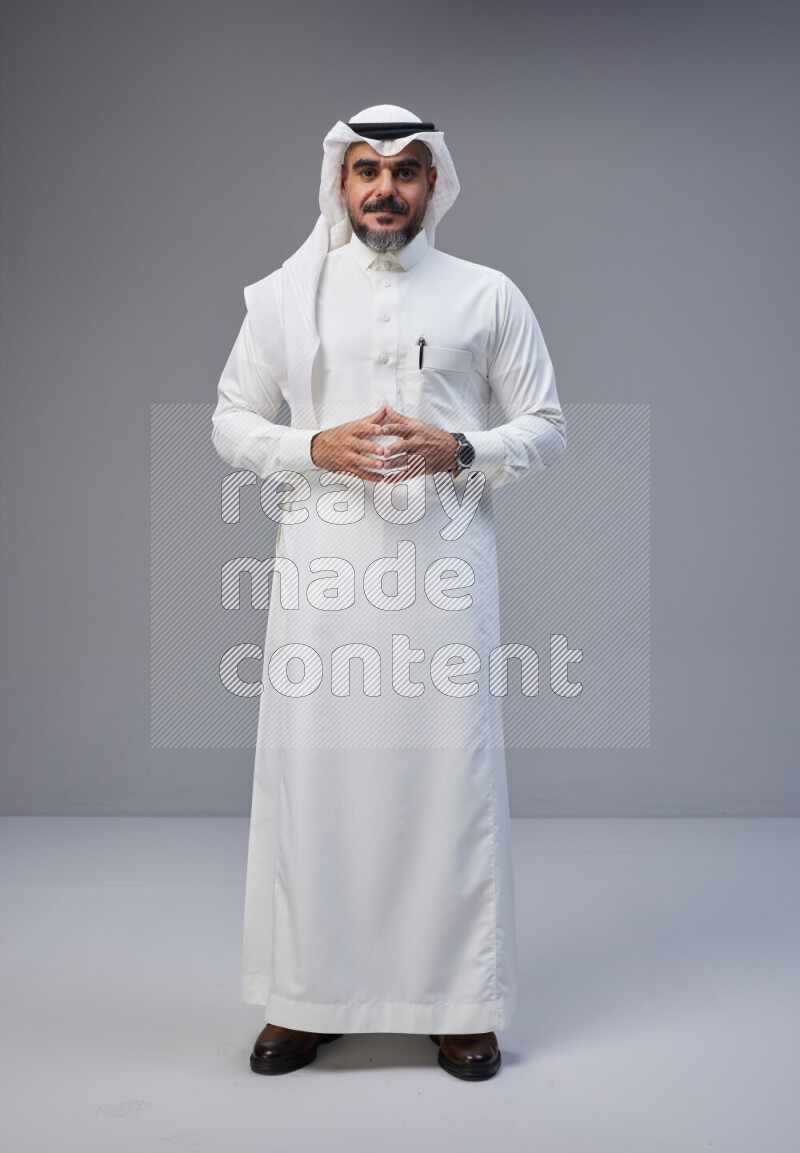 Saudi man Wearing Thob and white Shomag standing interacting with the camera on Gray background
