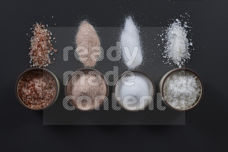 4 pottery bowls filled with himalayan salt and white salt on black background