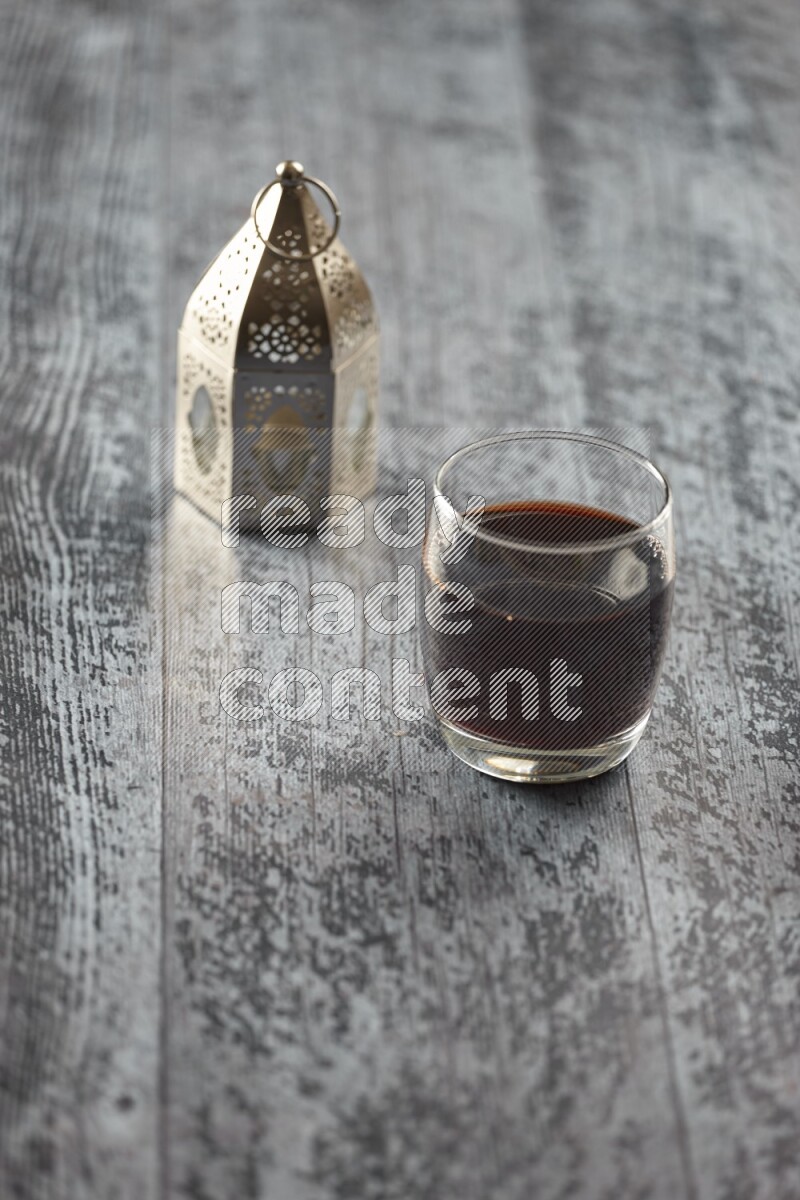 A silver lantern with different drinks, dates, nuts, prayer beads and quran on grey wooden background