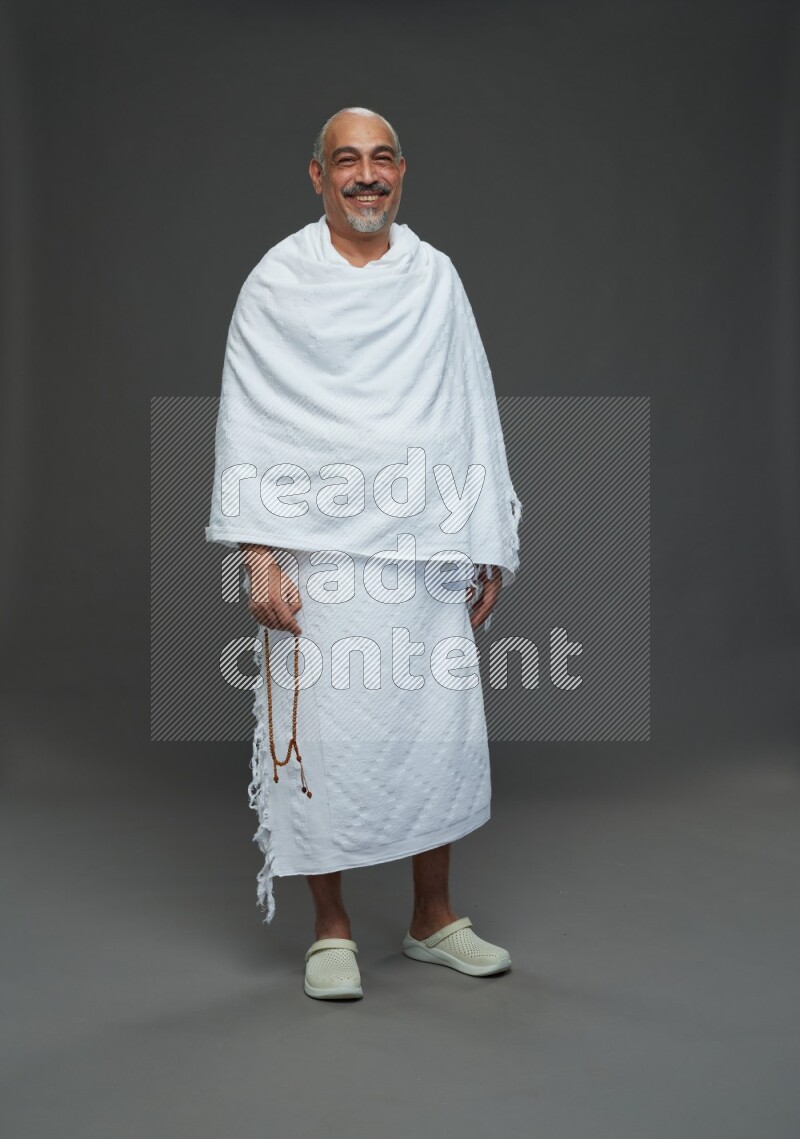 A man wearing Ehram Standing holding rosary on gray background