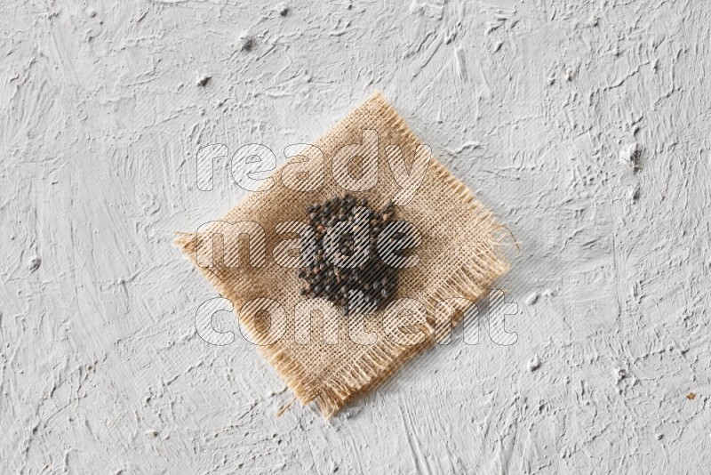 Black pepper on burlap fabric on a textured white flooring