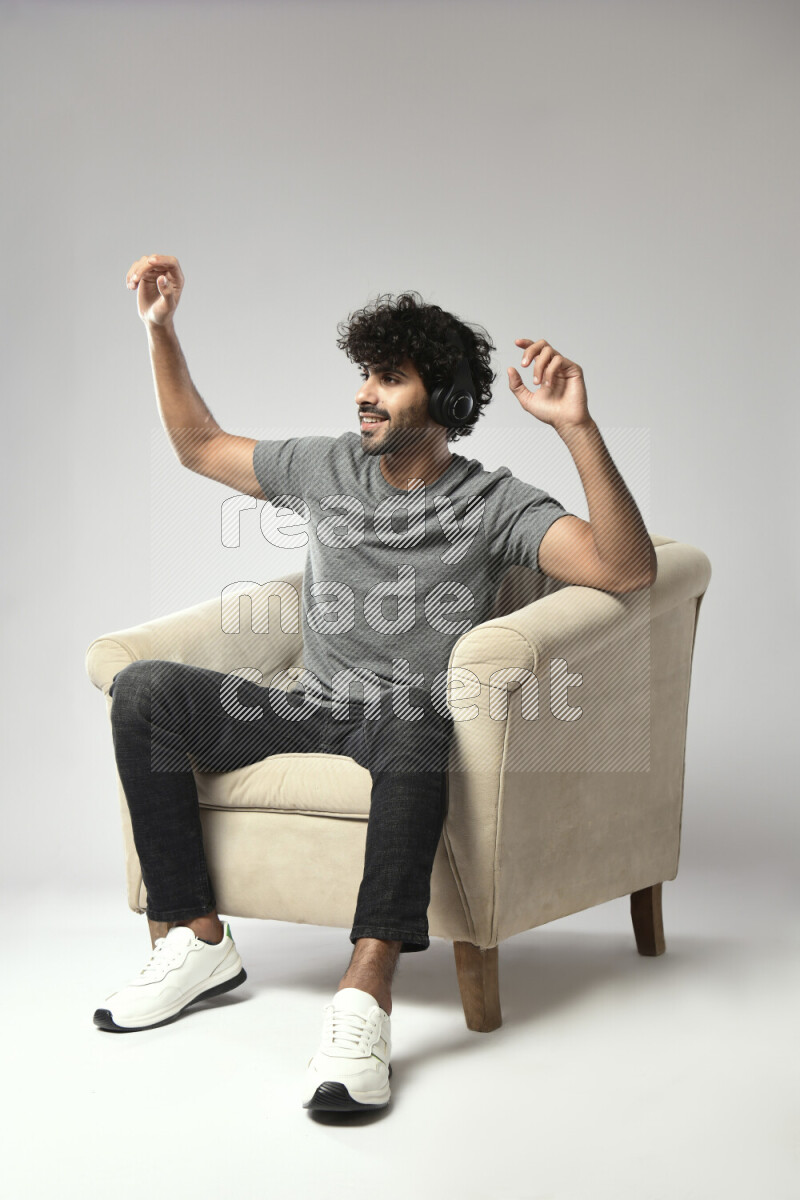 A man wearing casual sitting on a chair putting on headphones on white background