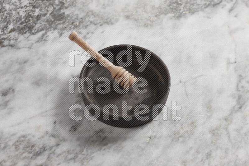 Black pottery oven plate with wooden honey dipper in it on grey marble background