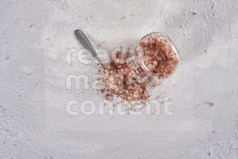 A glass jar full of coarse himalayan salt crystals on white background
