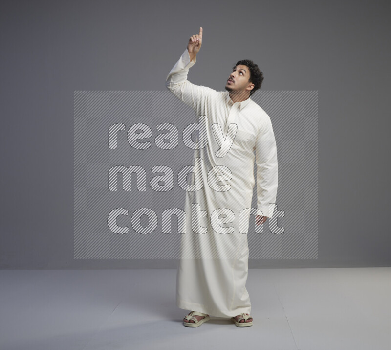 A Saudi man standing wearing thob interacting with the camera on gray background