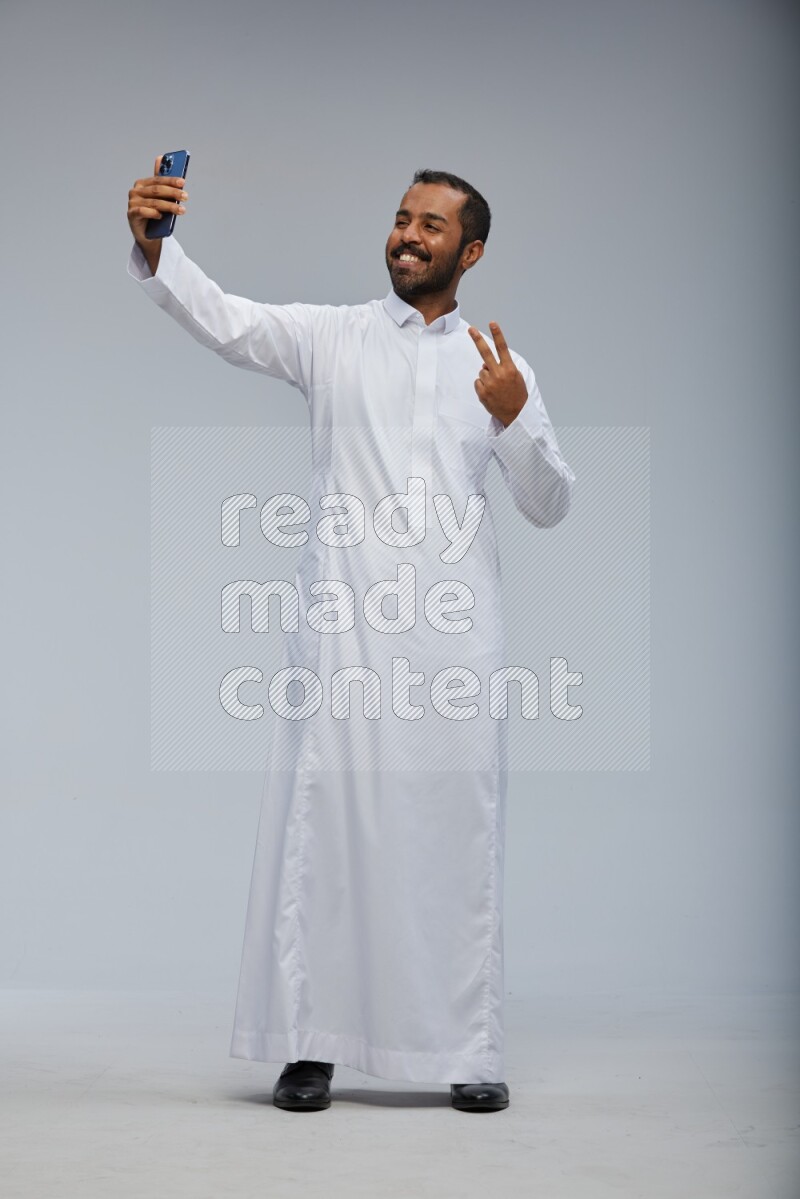 Saudi man wearing Thob standing taking selfie on Gray background