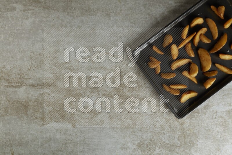 wedges potato in a black stainless steel rectangle tray on grey textured counter top