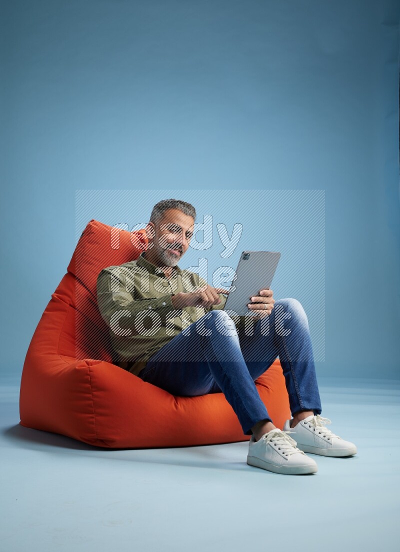 A man sitting on an orange beanbag and working on tablet