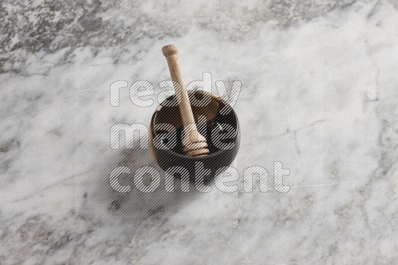 Multicolored pottery bowl with wooden honey dipper in it on grey marble background