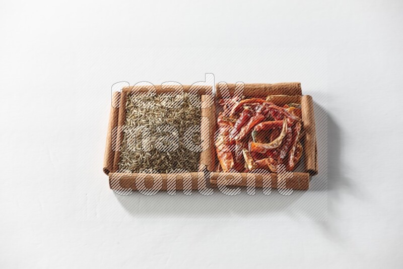 مربعان من أعواد القرفة ممتلئان بالفلفل الحار المجفف وحبوب الكمون علي خلفية بيضاء