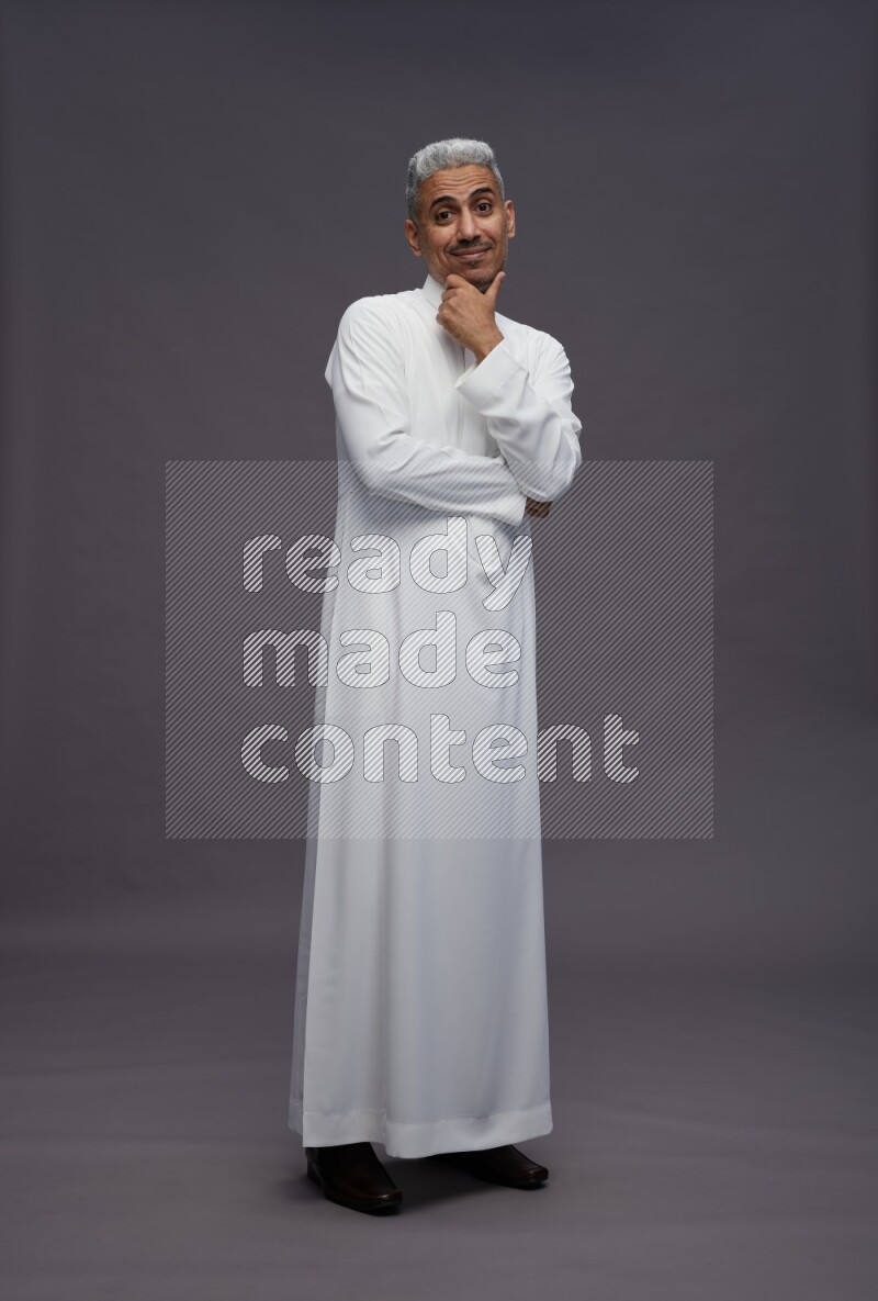 Saudi man wearing thob standing interacting with the camera on gray background