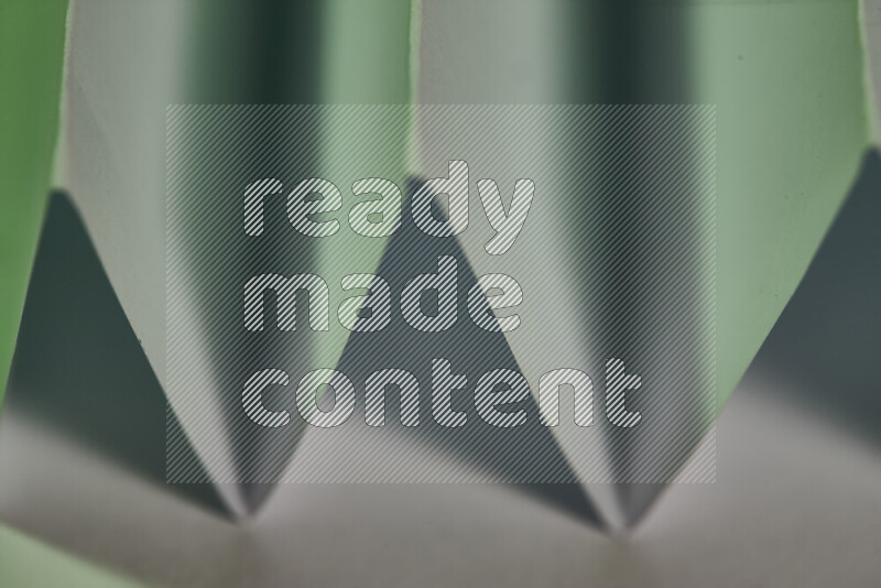 A close-up abstract image showing sharp geometric paper folds in white and green gradients