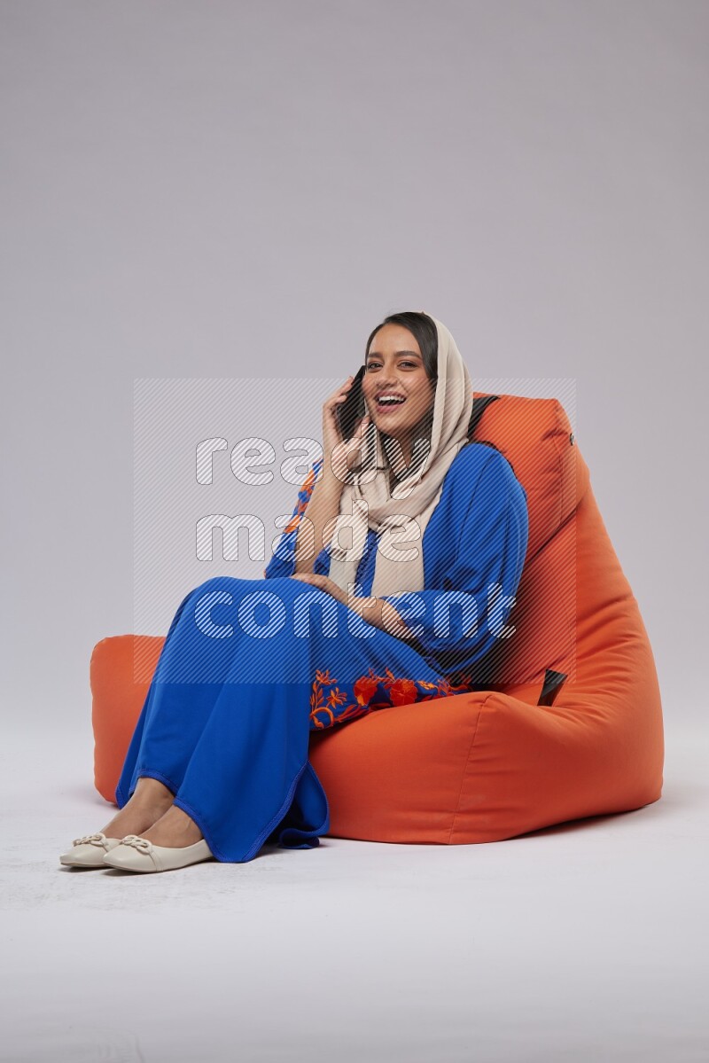 A Saudi woman wearing Jalabiya sitting on an orange beanbag and talking on the phone