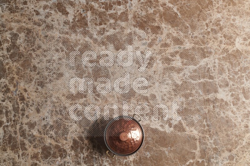 A small copper pot on beige marble background