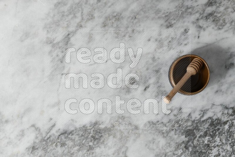 Multicolored pottery bowl with wooden honey dipper in it on grey marble background