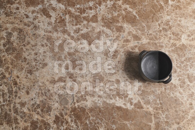 A black pottery bowl on beige marble background