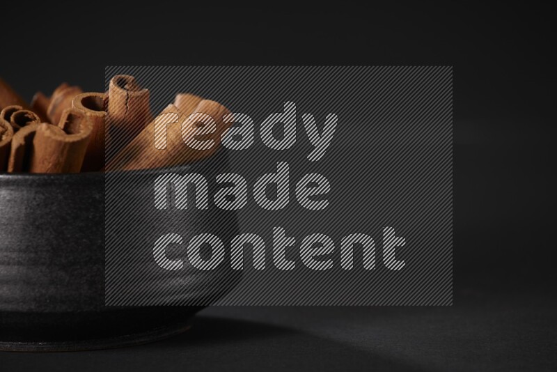 Cinnamon sticks in a black bowl on a black background in different angles