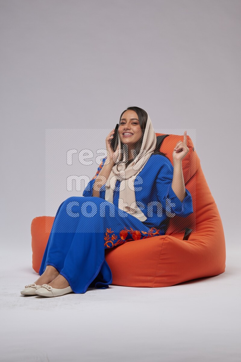 A Saudi woman wearing Jalabiya sitting on an orange beanbag and talking on the phone