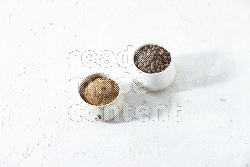2 beige bowls, one full of allspice powder and the other full of whole balls on a textured white flooring