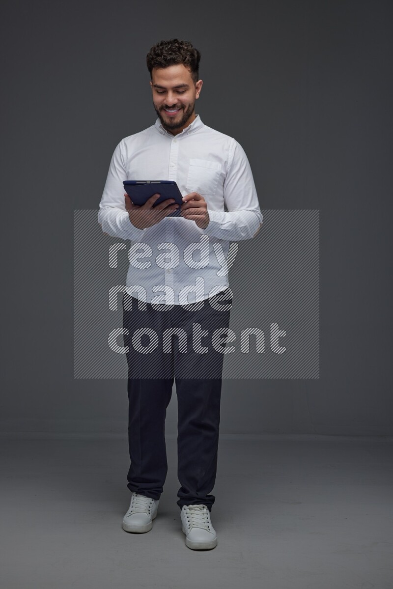 A man wearing smart casual standing and using his tablet eye level on a gray background