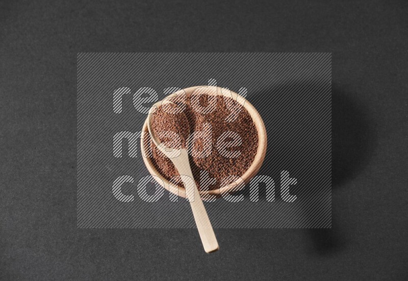 وعاء خشبي ممتلئ ببذور حب الرشاد وملعقة خشبية ممتلئة فوقه علي خلفية سوداء