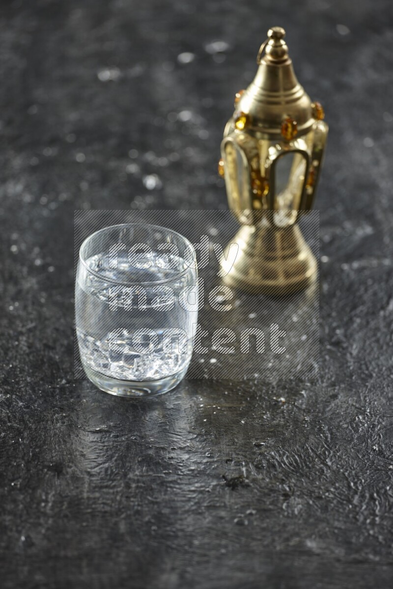 A golden lantern with different drinks, dates, nuts, prayer beads and quran on textured black background