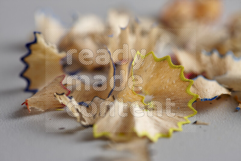 A close-up showing a small pile of pencil shavings with varied color edges on grey background