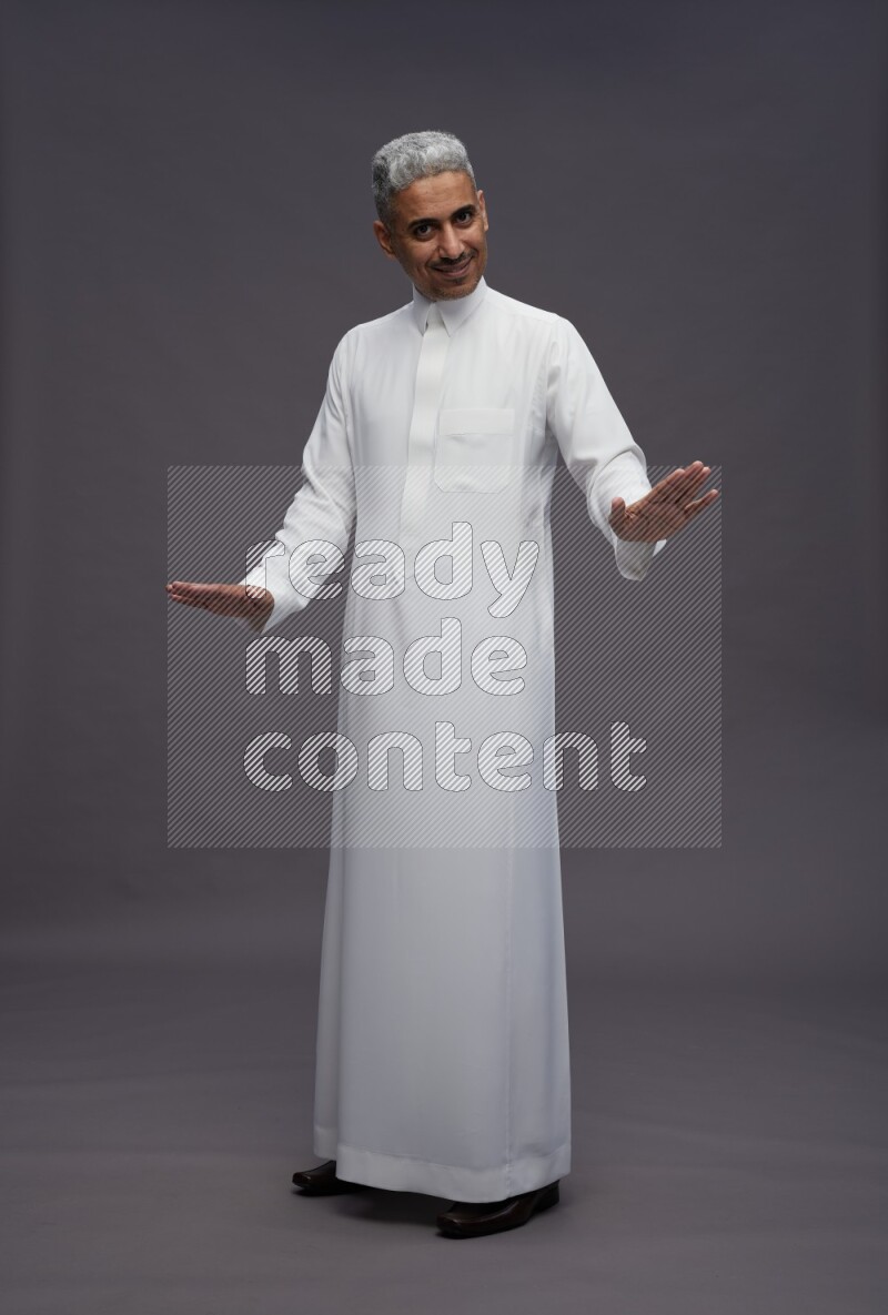 Saudi man wearing thob standing interacting with the camera on gray background