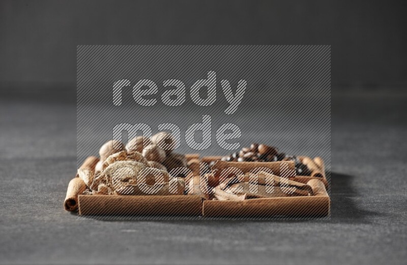 4 squares of cinnamon sticks full of coffee beans, cinnamon, dried ginger and nutmegs on black flooring