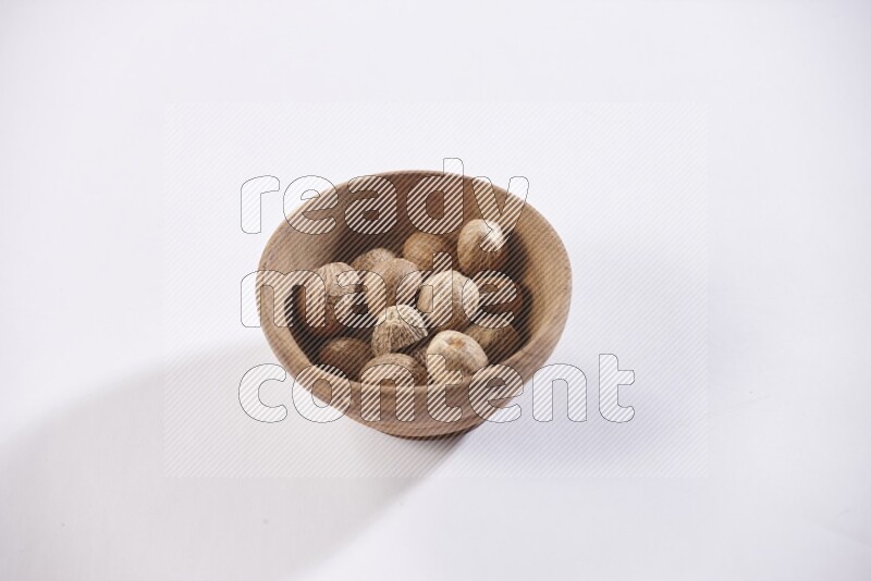 A wooden bowl full of whole nutmeg seeds on a white flooring