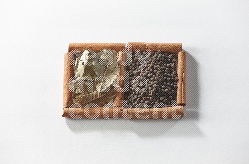 مربعان من أعواد القرفة ممتلئان بحبوب الفلفل الأسود وأوراق الغار علي خلفية بيضاء