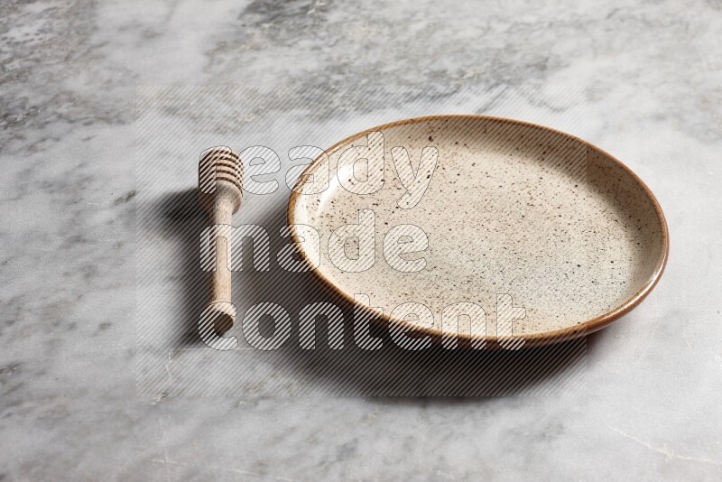 Multicolored pottery plate with wooden honey dipper on the side on grey marble background