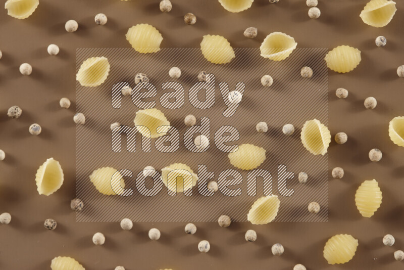 Raw pasta with different ingredients such as cherry tomatoes, garlic, onions, red chilis, black pepper, white pepper, bay laurel leaves, rosemary and cardamom on beige background
