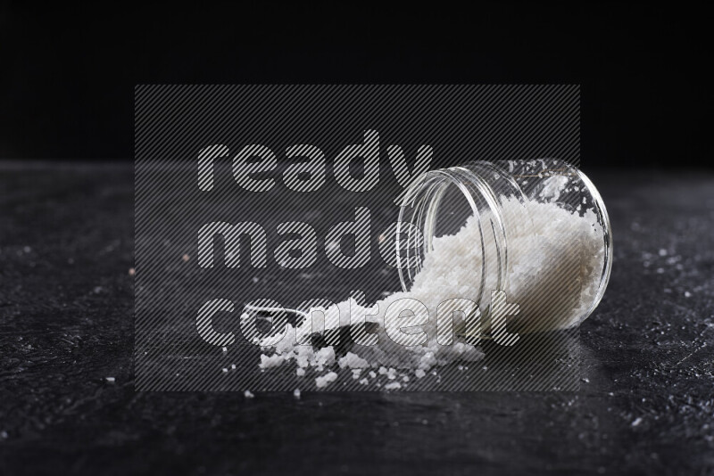 A glass jar full of coarse sea salt crystals on black background