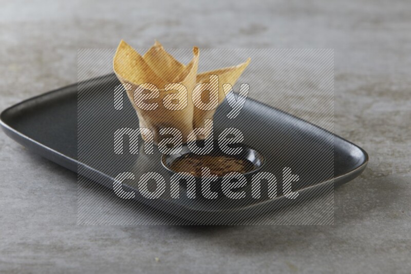 wonton cups with soy sauce ramkin on rectangle dark grey ceramic plate on grey textured counter top