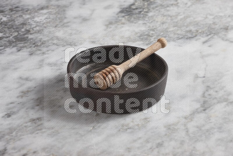 Black pottery oven plate with wooden honey dipper in it on grey marble background