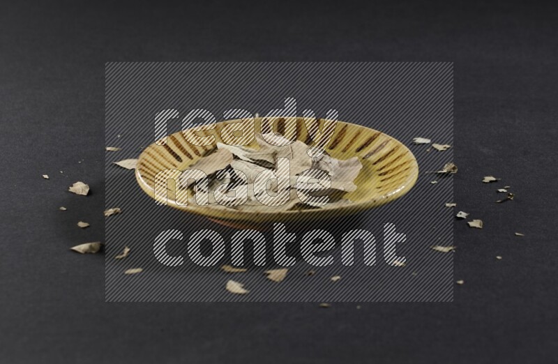 صحن فخاري متعدد الألوان ممتلئ بأوراق الغار المجففة على أرضية سوداء