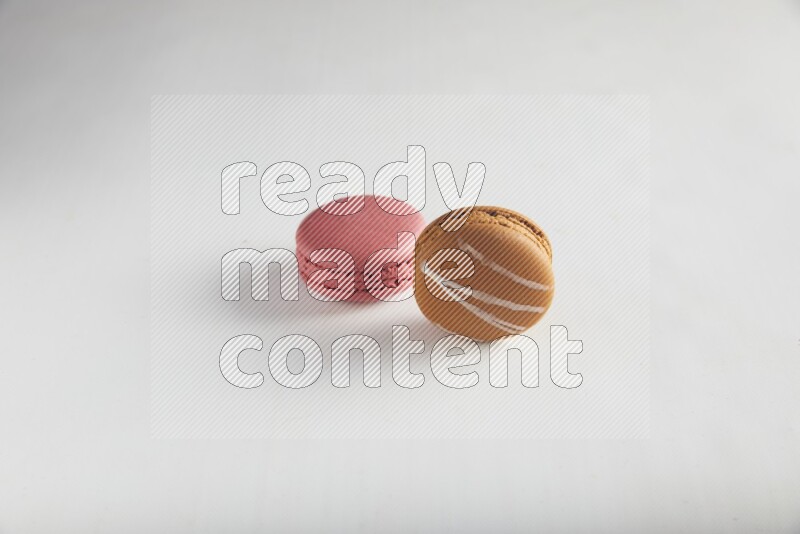 45º Shot of of two assorted Brown Irish Cream, and Pink Raspberry macarons on white background