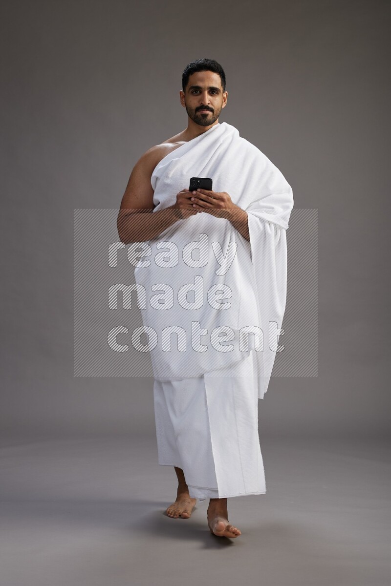 A man wearing Ehram Standing texting on phone on gray background