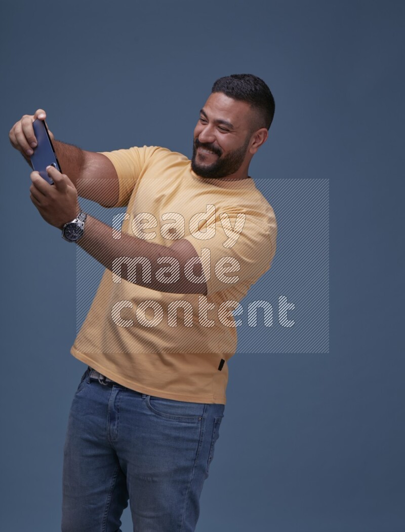 A man Playing Games on Smartphone on Blue Background wearing Orange T-shirt